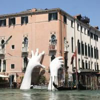 Sculpture of large white hands reaching out of water to support building