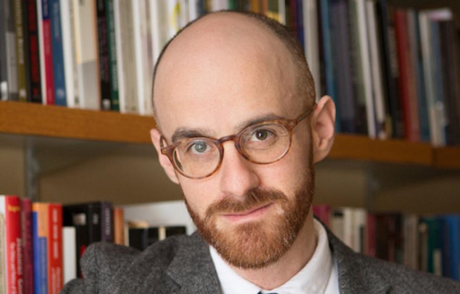 Alexander Livingston poses in front of a full bookshelf wearing orange-framed glasses