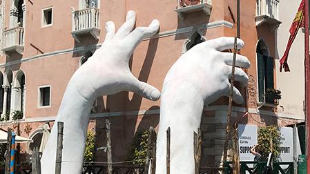 Large hand sculpture reaching out from water to hold building