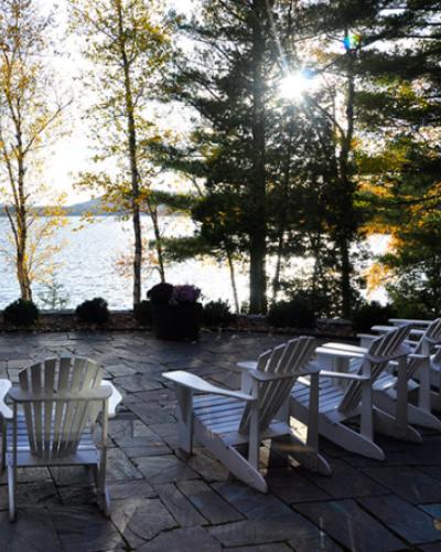 row of Adirondack chairs on a patio facing a lake