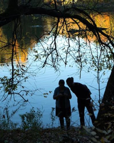 two silhouetted figures surrounded by trees in front of a lake